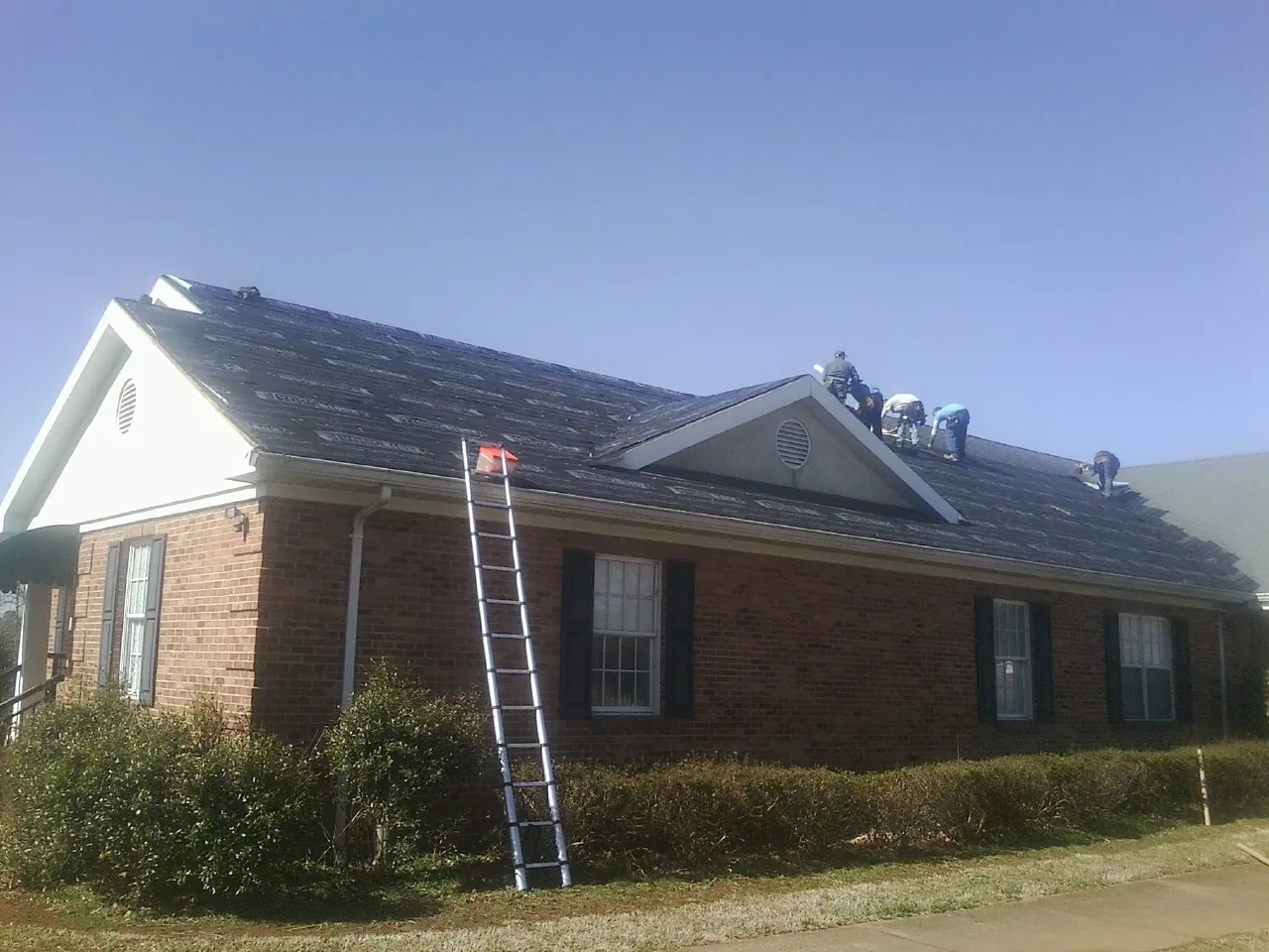 Crew tearing shingles off a brick ranch roof with a ladder set — Metal Roof Repair work by our crew in Markleville