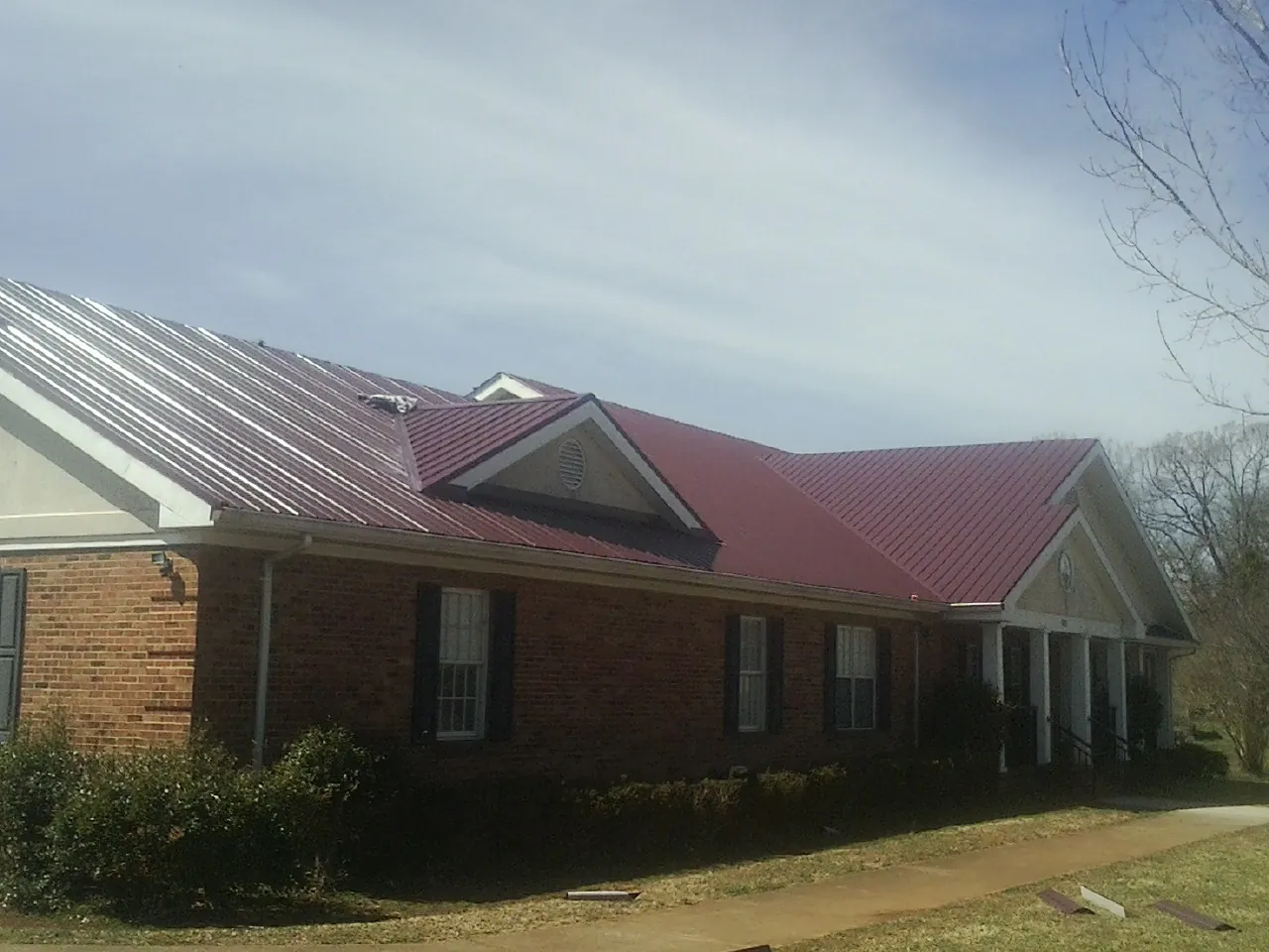 Red metal roof with gabled entries on a long brick building, from a Hail Damage Roof Repair job in Markleville