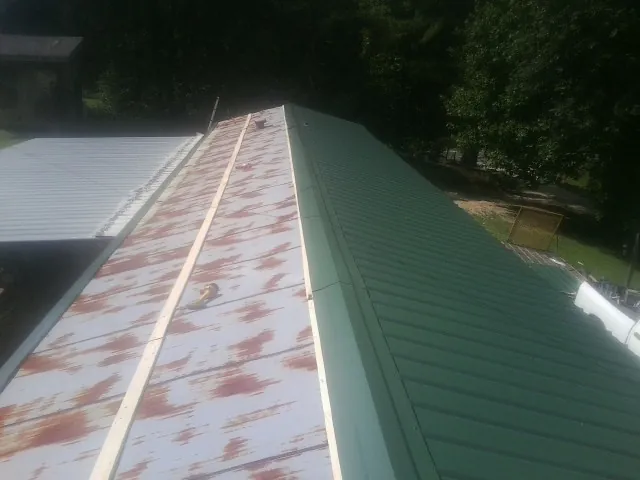 Old rusted panels beside newly installed green metal roofing — Wind Damage Roof Repair by Roofing Brothers in Markleville