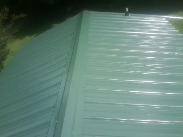 New green metal panels meeting at the ridge of a roof — Flat Roof Repair work by our crew in Markleville