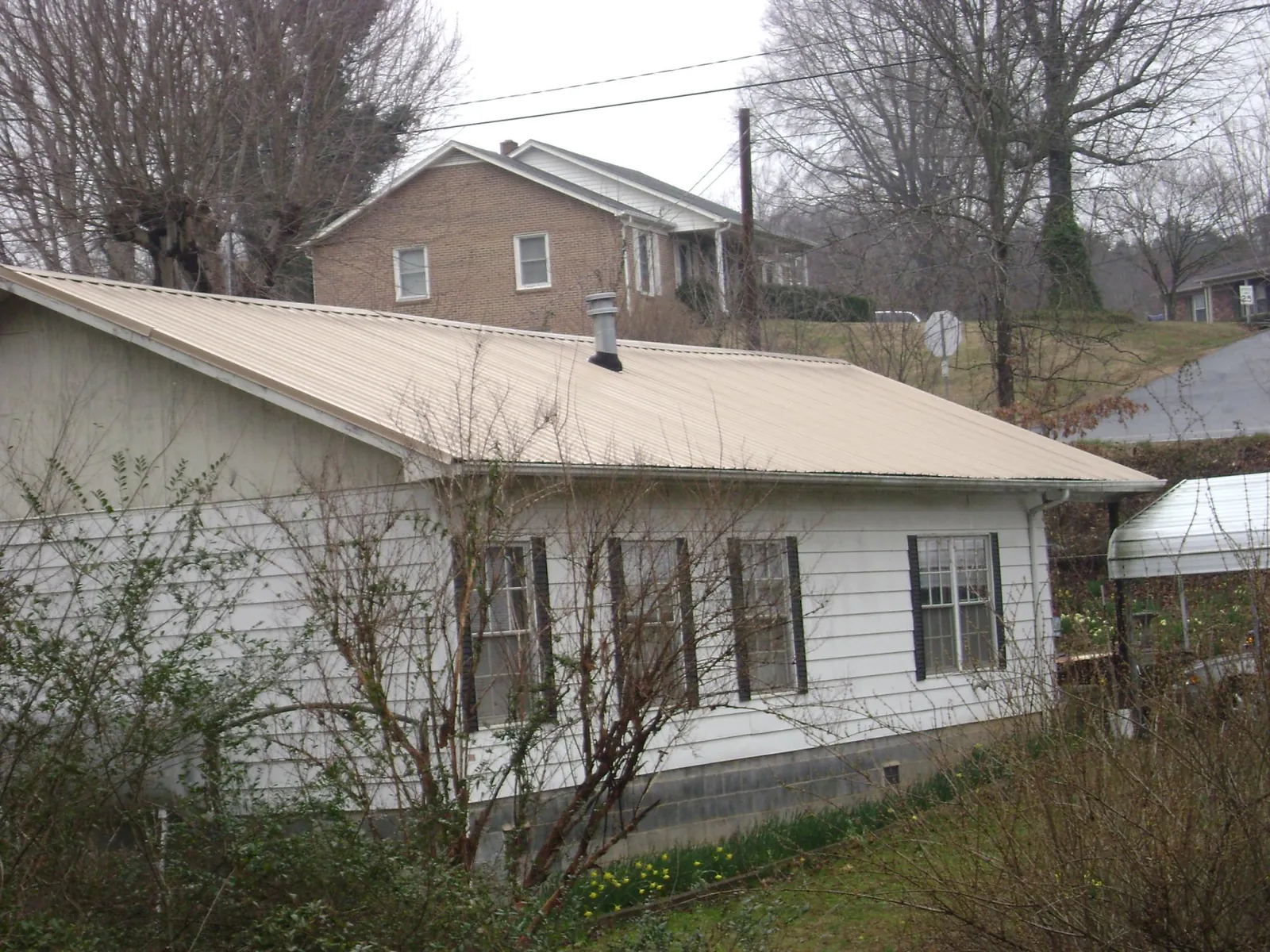 Tan metal roof on a white sided house set into a hillside — Commercial Roofing by Roofing Brothers in Markleville