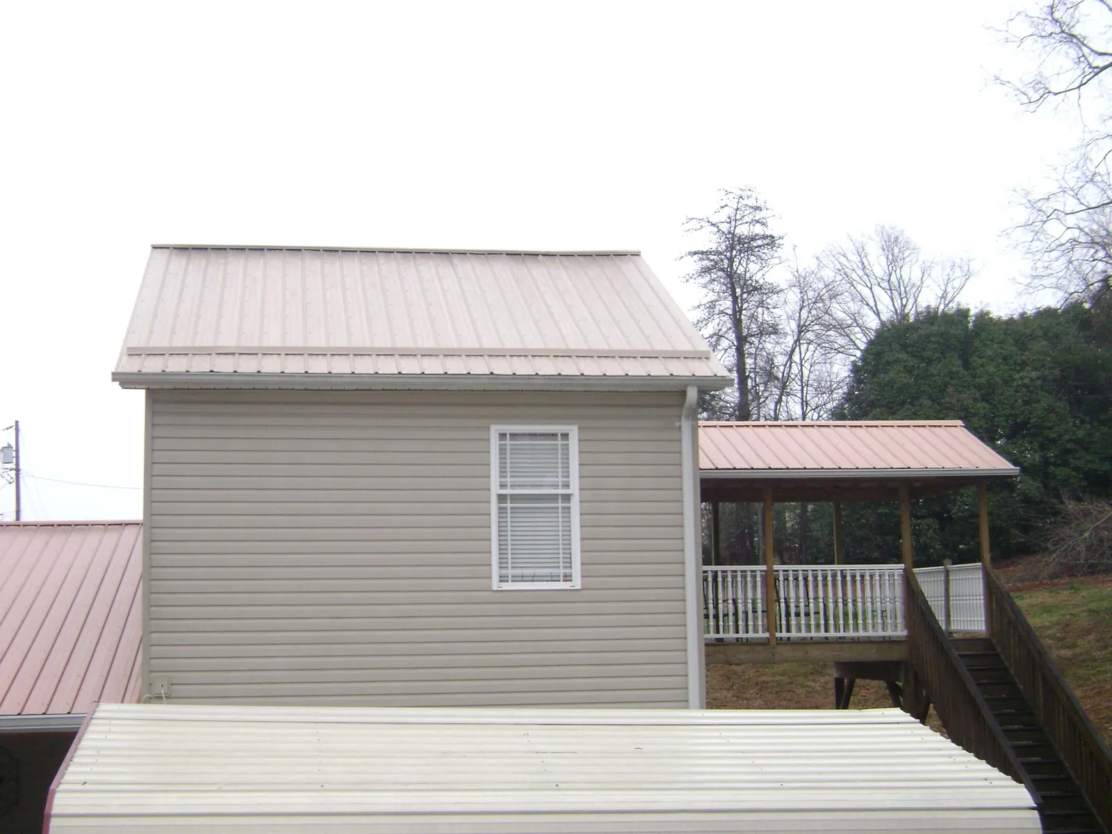 Tan metal roofs on a two story addition and attached porch, from a Roof Replacement job in Markleville